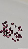 Multiple small, round, purple garnet cabochons shown under light on white background, displaying color, shape, and size.
