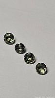 Four round cut moss green sapphires arranged in a line on a white background, showing size, color, and luster.