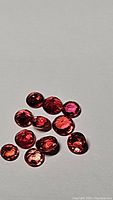Multiple small round-cut fire orange-red sapphires arranged in a cluster showing their deep rich coloration.