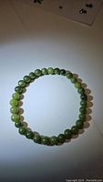 Natural green jade bead bracelet laid flat, showing round beads in various green hues