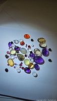 Mixed parcel of cut polished loose gemstones showing variety of colors and types including purple amethyst, yellow citrine, red rhodolite garnet, and black onyx.