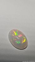 Close-up image showing the oval Ethiopian opal's play of color on a white background.