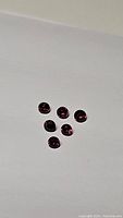 Six round deep red faceted stones on white background, top view