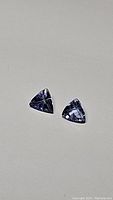 Pair of trillion-cut purple-blue tanzanite gemstones on gray background