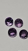 Four calibrated round checker cut natural Brazilian amethyst gemstones on neutral background, showing deep purple color and clarity.