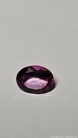 Oval cut natural hot pink topaz gemstone shown on a flat neutral surface, displaying facets and bright pink color from different angles.