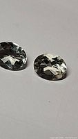 Pair of oval cut green amethyst gemstones with light teal color on white background, showing clarity and faceting details.