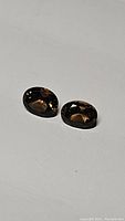 Two natural smokey quartz oval cut gemstones, clear visibility of cut and color, laid on a plain surface.