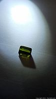 Rectangular cut green tourmaline gemstone placed on light background with illumination to show color and clarity.