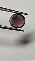 Close-up image of 1.25ct round step-cut untreated Myanmar spinel, deep purple-pink color, held with gemstone tweezers