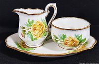 Photo showing full set of creamer, sugar bowl, and tray with detailed floral pattern and gold trim.