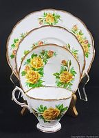 Front view of all four pieces stacked with cup in front showing the yellow rose pattern with gold trim.