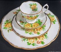 Top down view showing the stacked four-piece setting with cup, saucer, side plate, and dinner plate with yellow rose floral pattern, gold trim, and scalloped edges.