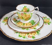 Photo of the 4 piece Tea Rose Yellow pattern dinnerware set by Royal Albert stacked and viewed from the front showing floral design and gold trim