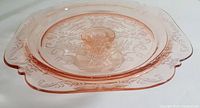 Angled front view showing overall design, color, and decorative pattern of pink Depression glass cake plate with pedestal.