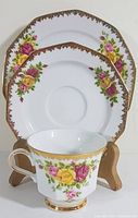 Demitasse cup positioned in front with saucer and side plate behind, showing detailed floral patterns and gold highlights on white porcelain.