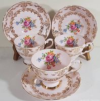 Set of three pink floral fine bone china teacups with matching saucers arranged side by side showing front floral motif and gold filigree detail.