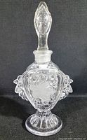 Full view of the clear glass perfume bottle with stopper showing teardrop shape and raised floral patterns.