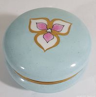 Top view of the vintage Limoges dresser jar lid showing pink and white flower design with gold outlining on light blue background.