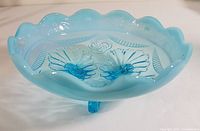 Blue opalescent glass footed dish with scalloped edge and embossed floral design, showing overall shape and pattern.