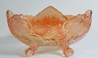 Side view of the oval footed marigold carnival glass centrepiece bowl showing embossed fruit and leaf patterns and scalloped edge with three legs.