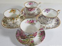 Four Royal Albert fine bone china teacups with matching saucers showing floral and scenic designs accented with gold trim.