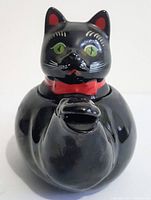 Front view of glossy black cat ceramic single cup teapot with red collar and green eyes showing the spout formed by cat's tail.