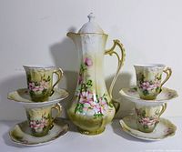 Overall photo of the complete tea set showing pot, cups stacked on saucers, floral hand painted design, and color tones.