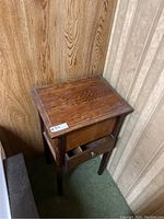 Small antique wooden night stand table with visible wear, scratches, and marks. One drawer partially open.