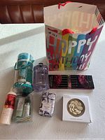 Gift bag and its contents including bath products, incense sticks, purple bottle, and incense holder on a table.