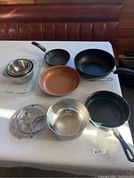 Top-down view of the assortment of pans, mixing bowls, glass bakeware and cooling rack displayed on a white tablecloth in natural light.