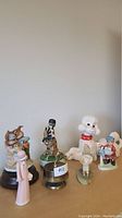 Six assorted porcelain and ceramic figurines displayed on a flat surface including animals and human figures.