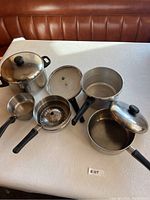 Overview of the assorted stainless steel pots, pressure cooker with lid, and vegetable steamer insert. All items on a table.