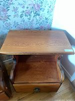 Photo showing front view of one wooden bedside table, highlighting drawer with metal ring pull and open shelf below tabletop