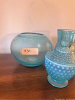 Two blue glass decor items: a round bubble glass bowl and a hobnail covered candy dish with lid shown on wooden surface.