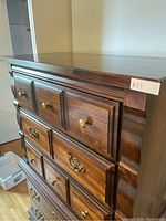 Front and partial side view of dark wood dresser showing drawer fronts with brass and gold-colored handles and raised panel drawer fronts.