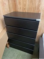 Front view of the black wood dresser with five drawers, showing the drawer fronts and top surface.