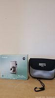 Canon PowerShot ELPH 300HS boxed next to black Roots carrying case.