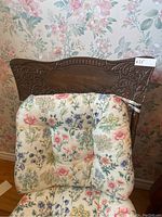 Front view of the antique dark wood rocking chair showing the carved backrest and floral patterned cushions on seat and back.