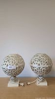 Pair of white round decorative lamps showing scrollwork globe on square bases with cords.