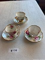 Three Royal Albert teacups and saucers displayed on table, showing floral patterns and gold trim.