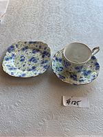 Photo showing Royal Albert china set including teacup, saucer, and square plate with blue floral pattern on white background, placed on textured white tablecloth.