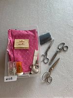 Top down image showing the lot contents inside a plastic container, including pink cotton fabric, sewing threads, measuring tape, and scissors.
