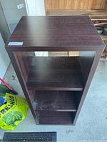 Front view of dark brown wooden shelf unit showing three compartments and flat top surface.