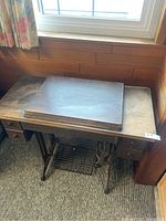 Full view of the antique Singer sewing machine with the wooden sewing table and treadle base visible.