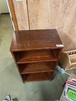 Top view of a compact wooden bookshelf with three shelves, showing wood grain and some surface wear.