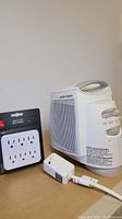 Photo showing Black and Decker small heater/fan unit with a carry handle and an off-white multi plug with 8 outlets.