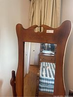 Angle view of wooden standing mirror highlighting the base support legs and detail of wood grain and cutout on top frame.