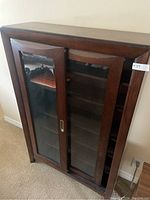 Front view of wooden storage bookcase with two sliding glass panel doors, showing shelving inside.
