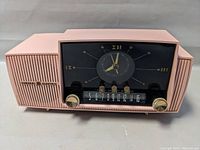 Front angle of the pink General Electric tube clock radio showing clock face, knobs, and speaker grille.